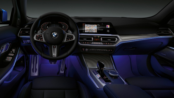 BMW Série 3 Berline, éclairage d’ambiance Vue de face du poste de conduite côté conducteur de la BMW Série 3 Berline avec espace aux pieds baigné de lumière bleue diffusée par l’éclairage d’ambiance