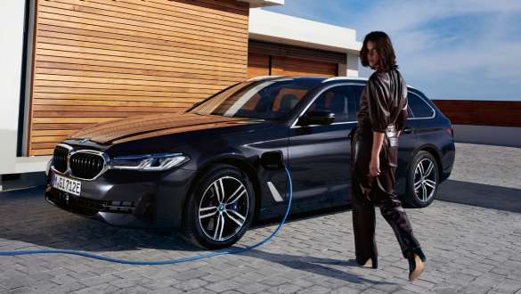 BMW Série 5 Touring hybride rechargeable 2021 G31, vue de trois quarts de profil branchée à une borne de recharge BMW Série 5 Touring hybride rechargeable 2021 G31, vue de trois quarts de profil branchée à une borne de recharge avec modèle