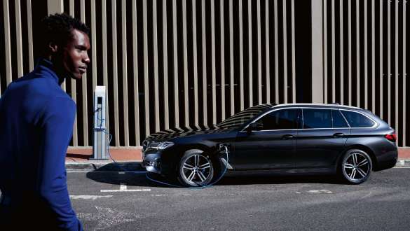 BMW Série 5 Touring hybride rechargeable 2021 G31, vue de profil branchée à une borne de recharge BMW Série 5 Touring hybride rechargeable 2021 G31, vue de profil branchée à une borne de recharge avec modèle