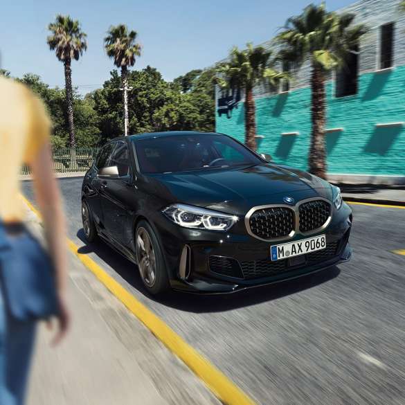 BMW M135i xDrive, vue de trois quarts avant F40. BMW M135i xDrive en Saphirschwarz metallic, vue de trois quarts avant, avec femme à l’avant-plan F40.
