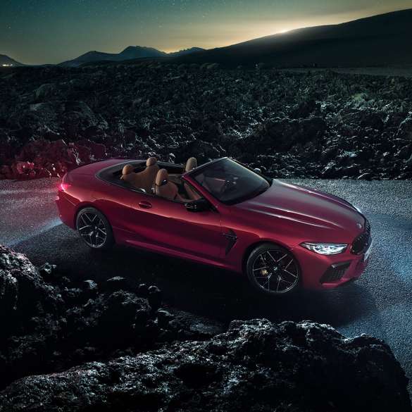 BMW M8 Competition Cabrio, vue de trois quarts de profil F91. BMW M8 Competition Cabrio en Motegi Rot metallic avec capote ouverte, vue de trois quarts de profil, à l’arrêt sur l’asphalte pendant la nuit F91.