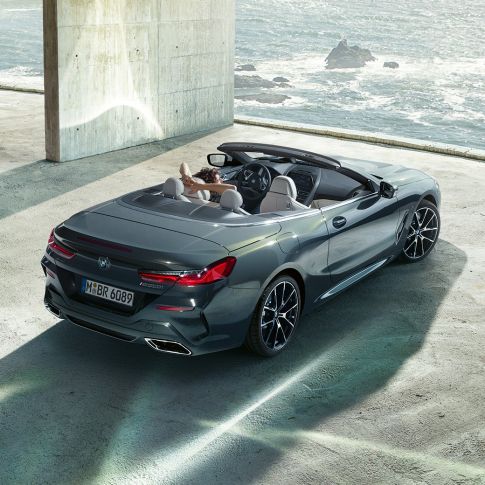 BMW M850i xDrive Cabrio, vue en plongée G14. BMW M850i xDrive Cabrio en Dravitgrau metallic avec capote ouverte, vue en plongée, en stationnement dans un bâtiment en béton devant l’océan G14.
