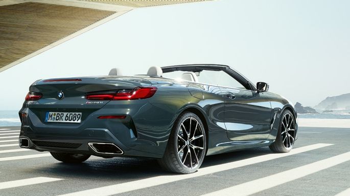 BMW M850i xDrive Cabrio, vue de trois quarts arrière G14. BMW M850i xDrive Cabrio en Dravitgrau metallic avec capote ouverte, vue de trois quarts arrière, en stationnement avec vue sur l’océan G14.