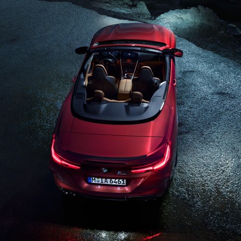 BMW M8 Competition Cabrio, vue en plongée F91. BMW M8 Competition Cabrio en Motegi Rot metallic avec capote ouverte, à l’arrêt sur l’asphalte, vue en plongée nocturne F91.