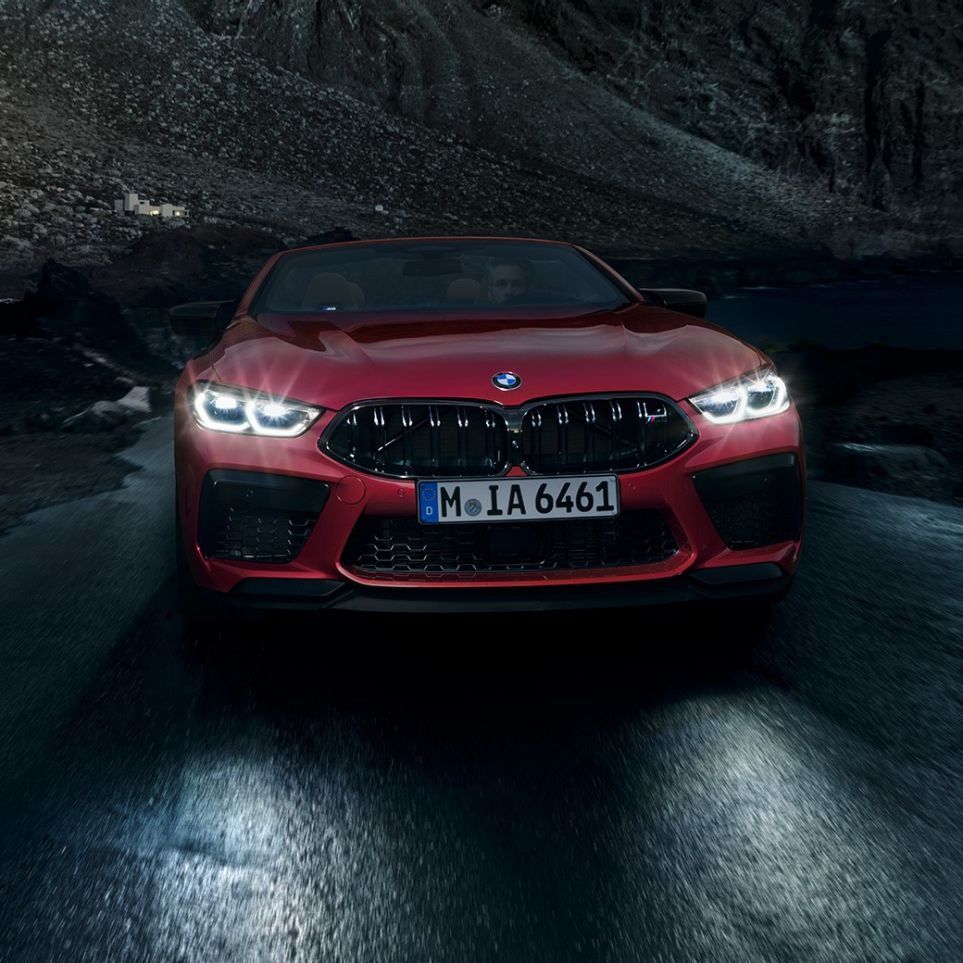 BMW M8 Competition Cabrio, vue avant F91. BMW M8 Competition Cabrio en Motegi Rot metallic avec phares allumés, vue avant, en conduite de nuit F91.