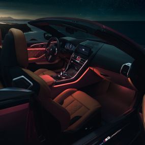BMW M8 Competition Cabrio, habitacle F91. BMW M8 Competition Cabrio avec capote ouverte, prise de vue nocturne de l’habitacle avec éclairage d’ambiance rouge F91.