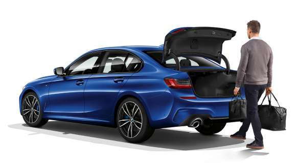 BMW 3 Reeks Berline (G20), automatische achterklepbediening. Driekwart achteraanzicht van de BMW 3 Reeks Berline (G20) in stilstand met bestuurder, die de achterklep automatisch opent met de voet.