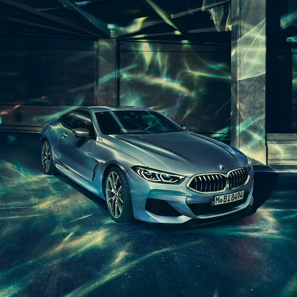 BMW M850i xDrive Coupé, driekwart vooraanzicht links G15. BMW M850i xDrive Coupé in Barcelona Blau metallic, driekwart vooraanzicht links, stilstaand voor gebouw G15.