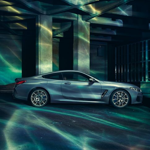 BMW M850i xDrive Coupé, zijaanzicht G15. BMW M850i xDrive Coupé in Barcelona Blau metallic, zijaanzicht stilstaand voor gebouw G15.