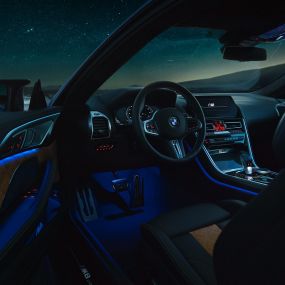 Interieur BMW M8 Competition Coupé F92. BMW M8 Competition Cabrio, interieur ‘s nachts met lederen M stuur en blauwe sfeerverlichting met geopende bestuurdersdeur F92.