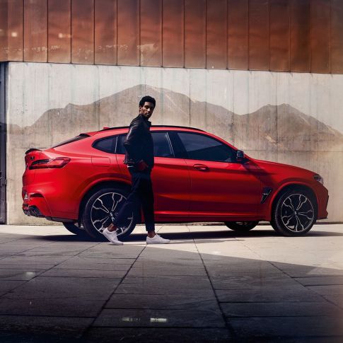 BMW X4 M Competition, zijaanzicht met jonge man F98. BMW X4 M Competition in Toronto Rot metallic, exterieur, zijaanzicht met jonge man F98.