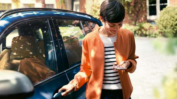 Vrouw kijkt op haar smartphone en opent de deur van haar BMW BMW Teleservices vrouw kijkt op haar smartphone en opent de deur van haar BMW