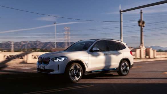 Adaptieve M ophanging BMW iX3 G08 rijdend op de weg Adaptieve M ophanging BMW iX3 G08 2020 Mineralweiß metallic driekwart vooraanzicht rijdend op de weg
