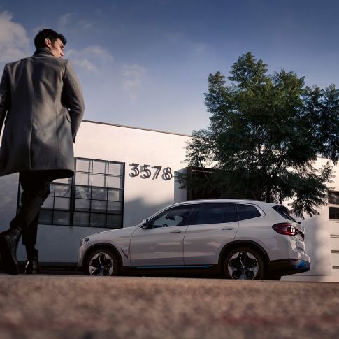 BMW iX3 G08 zijaanzicht voor gebouw met man BMW iX3 G08 2020 Mineralweiß metallic zijaanzicht voor gebouw met man