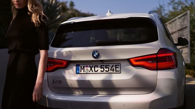 Achterkant met BMW i specifieke diffusor BMW iX3 G08 achteraanzicht met vrouw Achterkant met BMW i specifieke diffusor BMW iX3 G08 2020 Mineralweiß metallic achteraanzicht met vrouw