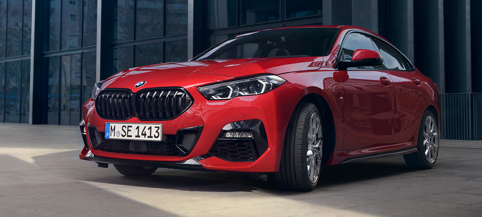 BMW Série 2 Gran Coupé F44 M135i, vue de trois quarts avant Edition ColorVision Melbourne Rot metallic BMW Série 2 Gran Coupé F44 M135i, vue de trois quarts avant Edition ColorVision Melbourne Rot metallic devant un bâtiment