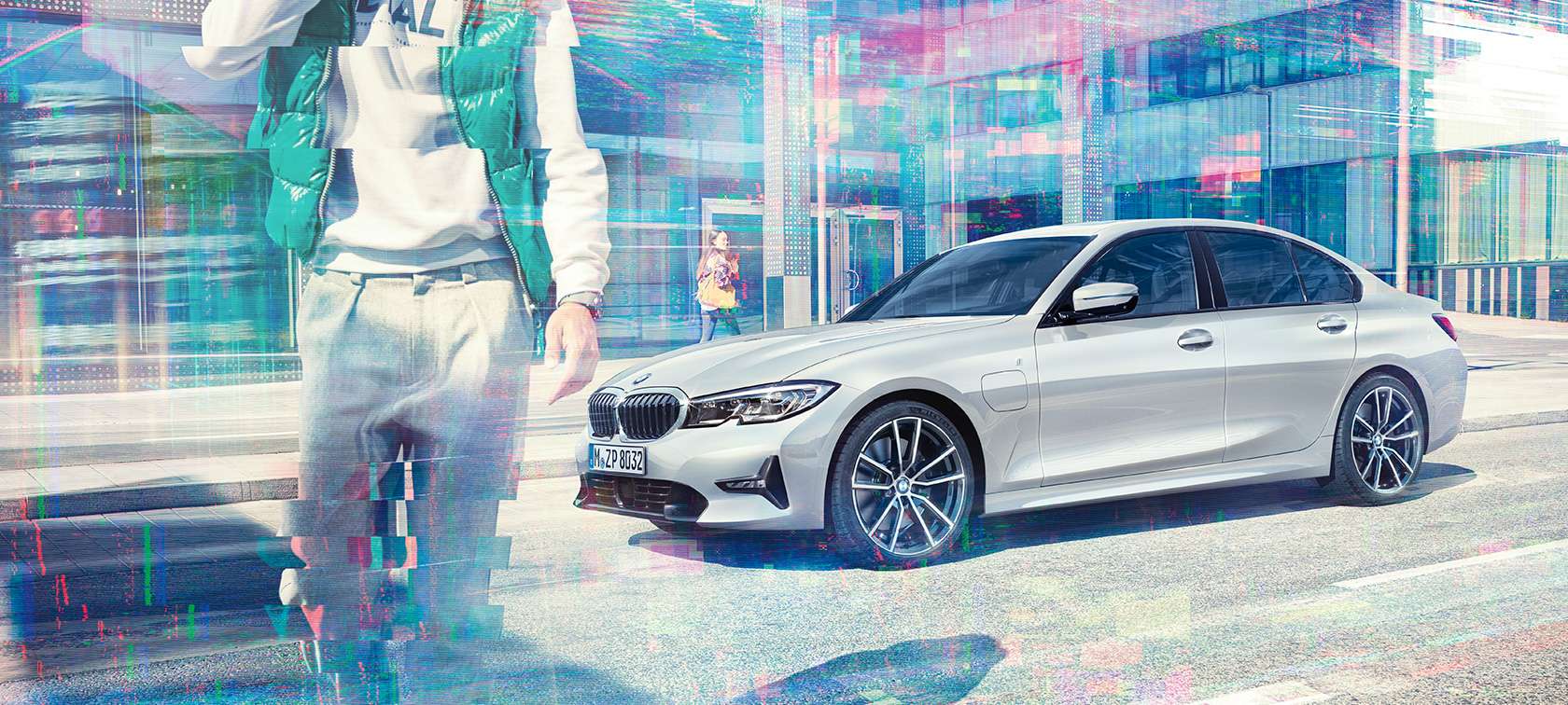 BMW 3 Reeks Berline, zijaanzicht BMW 330e G20. Driekwart zijaanzicht van de stilstaande BMW 330e Berline tegen een achtergrond met glazen gevels in de stad met voorbijgangers G20.