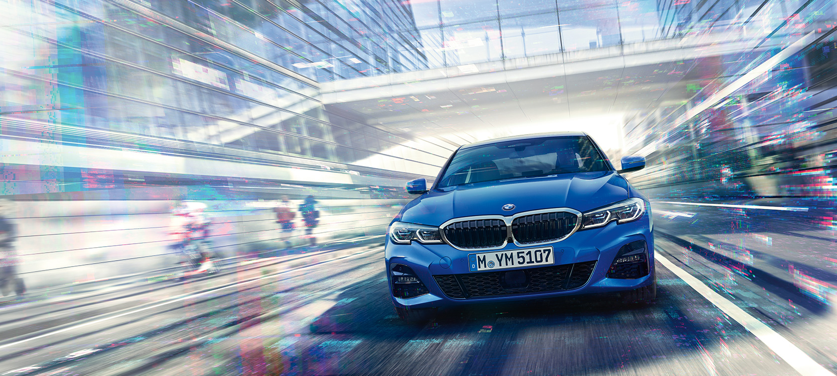 BMW Série 3 Berline, vue de face Vue de face de la BMW Série 3 Berline en mouvement de jour sous des immeubles de verre.