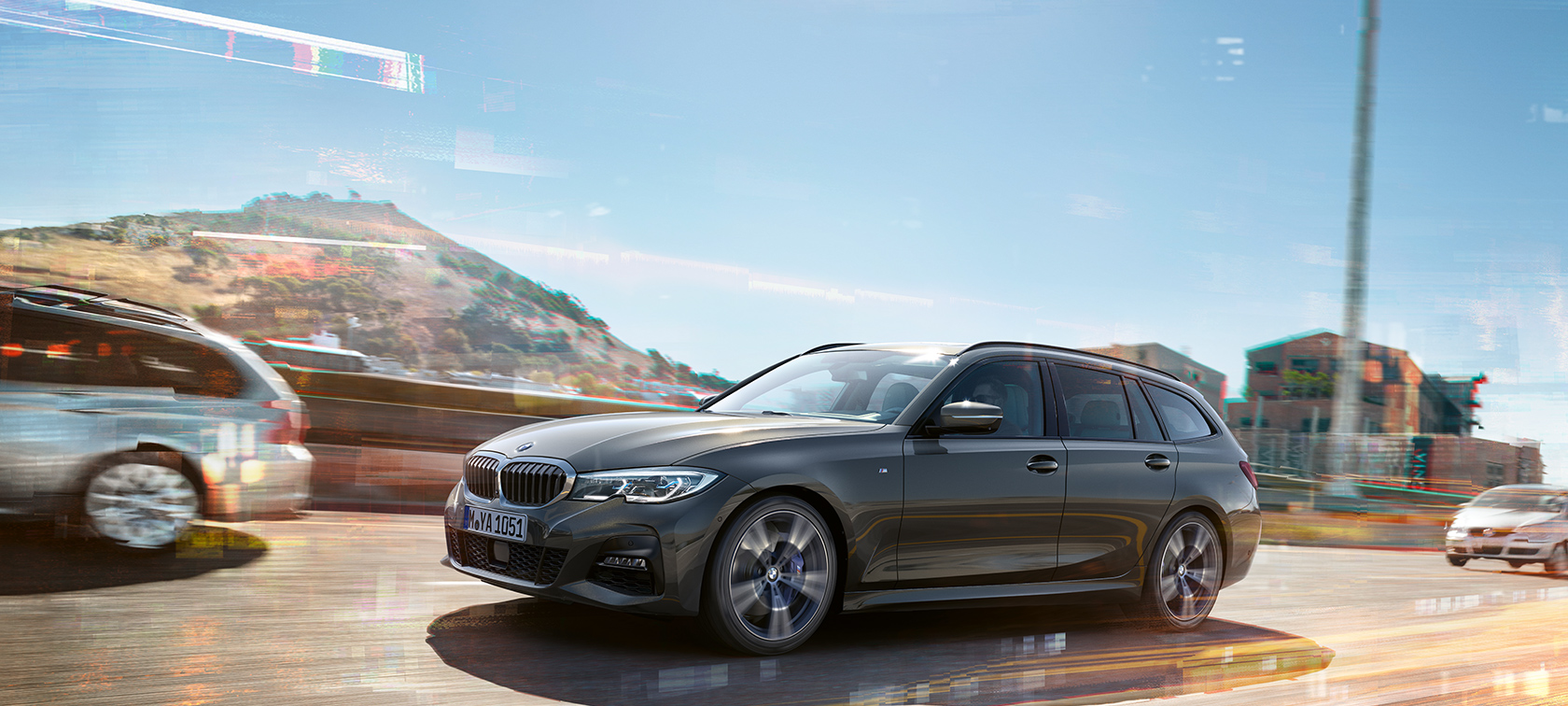 BMW 3 Series Touring, lateral driving shot G21 BMW 3 Series Touring, lateral driving shot in front of houses and mountains in the background G21