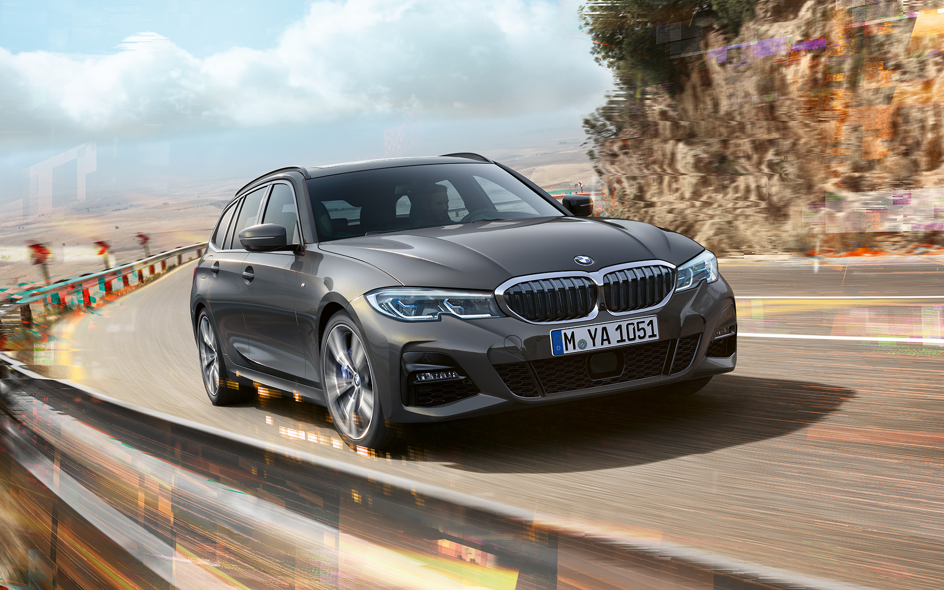 BMW Série 3 Touring (G21), vue de trois quarts avant design BMW Série 3 Touring (G21) Dravitgrau en marche, vue de trois quarts avant sur un pont devant un environnement rural