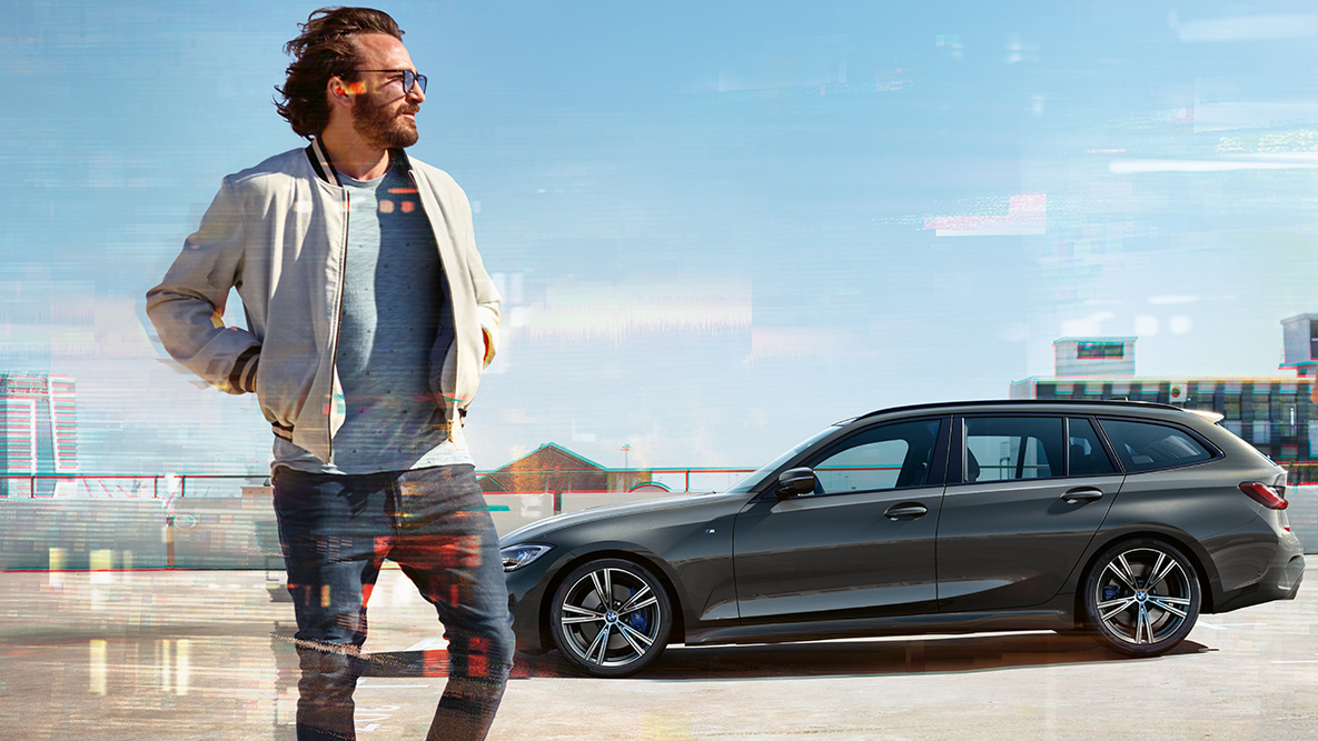 BMW 3 Reeks Touring (G21), driekwart vooraanzicht design BMW 3 Reeks Touring (G21) Dravitgrau, driekwart vooraanzicht tijdens het rijden op een brug in een landelijke omgeving