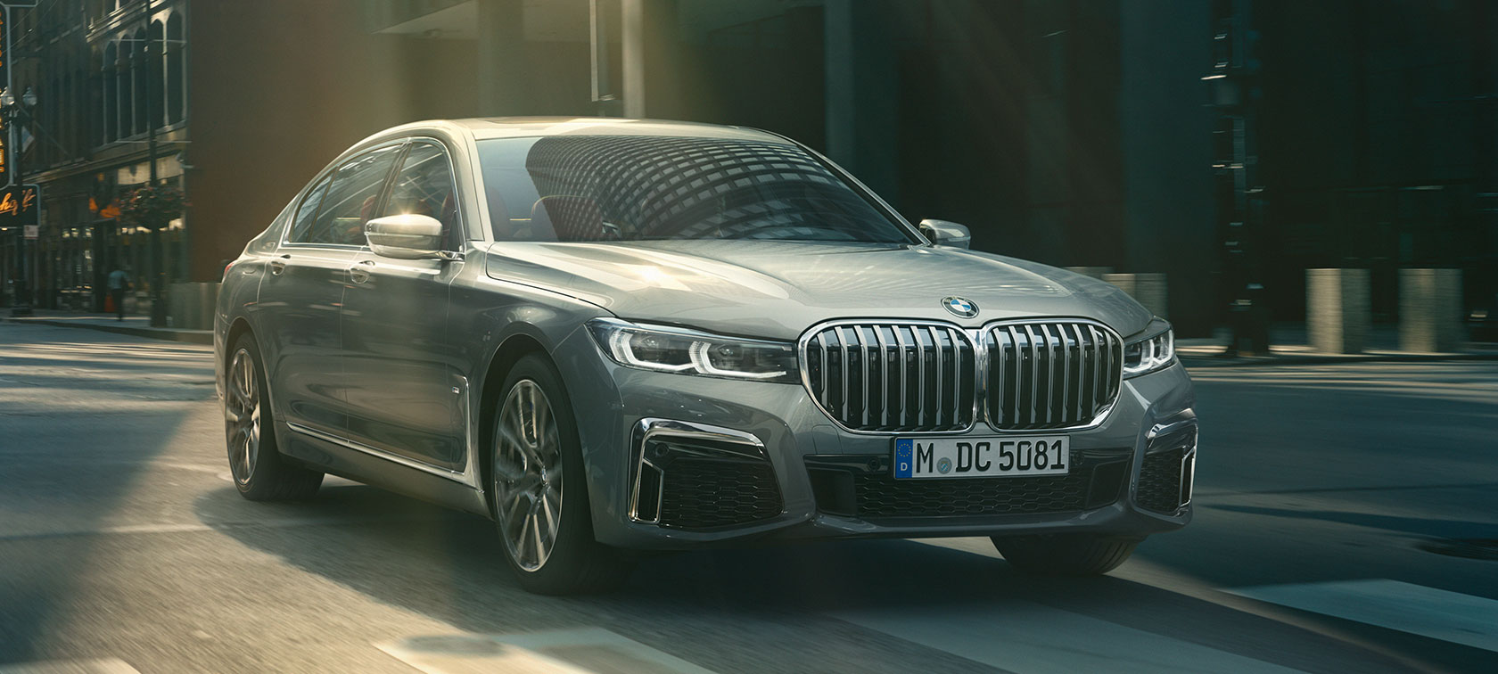 Grijze BMW 7 Reeks rijdend, driekwart vooraanzicht G11 Grijze BMW 7 Reeks rijdt in driekwart vooraanzicht door stedelijke omgeving G11
