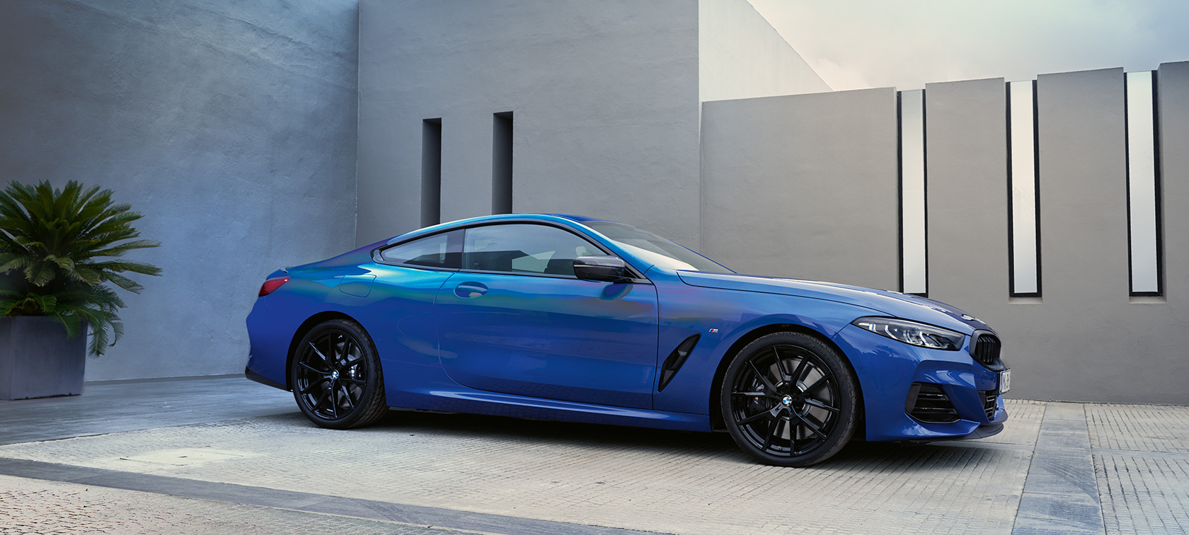 BMW 8 Reeks Coupé G15 LCI facelift 2022 M Portimao Blau metallic zijaanzicht stilstaand voor huismuur