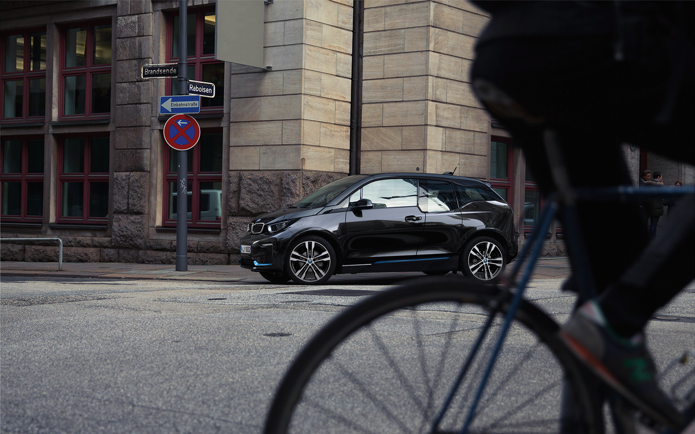 BMW i3s I01 voiture électrique 2018, vue de profil BMW i3s I01 voiture électrique 2018 en Fluid Black avec accent BMWi Blau vue de profil en mouvement dans un décor urbain