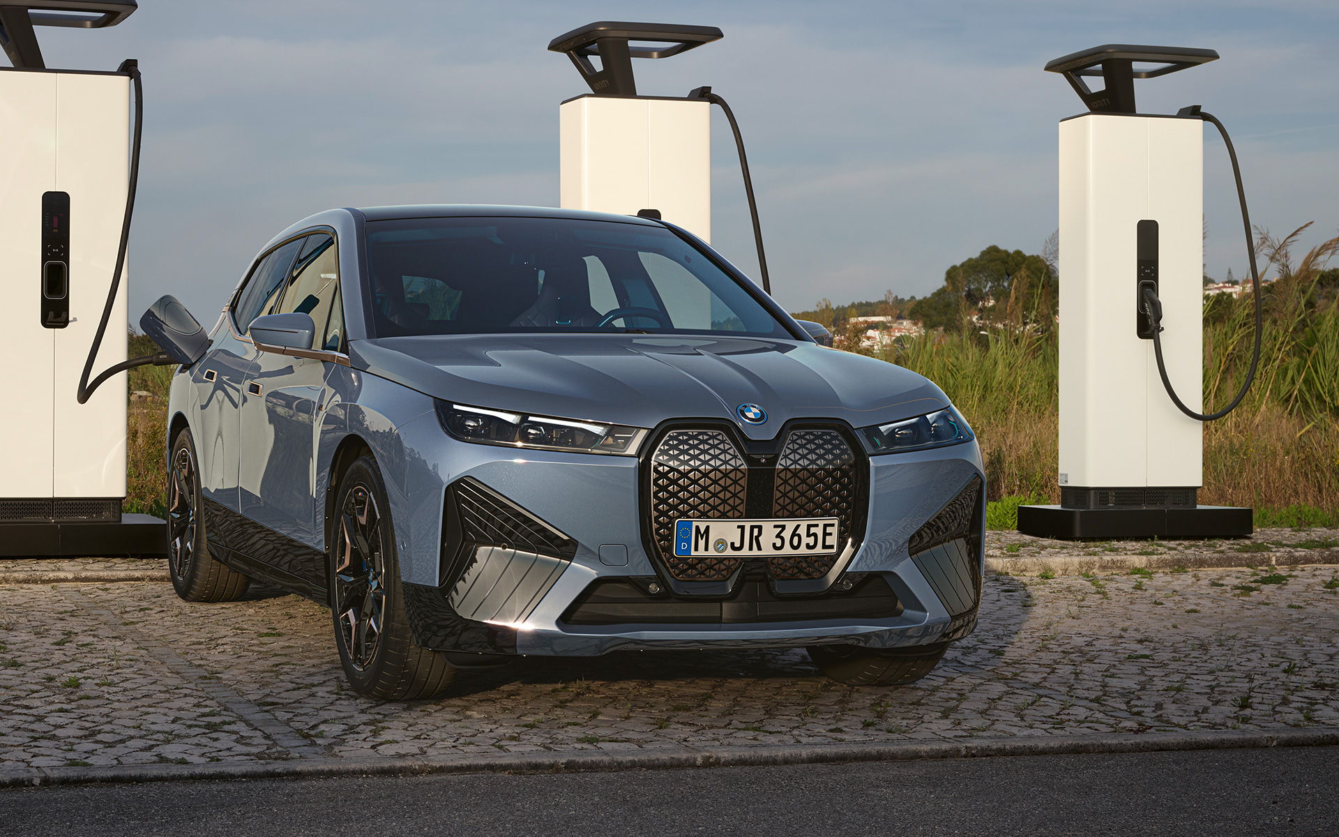 BMW iX M60 i20 2022 elektrische SUV BMW Individual Storm Bay metallic vooraanzicht aan High Power Charging-station