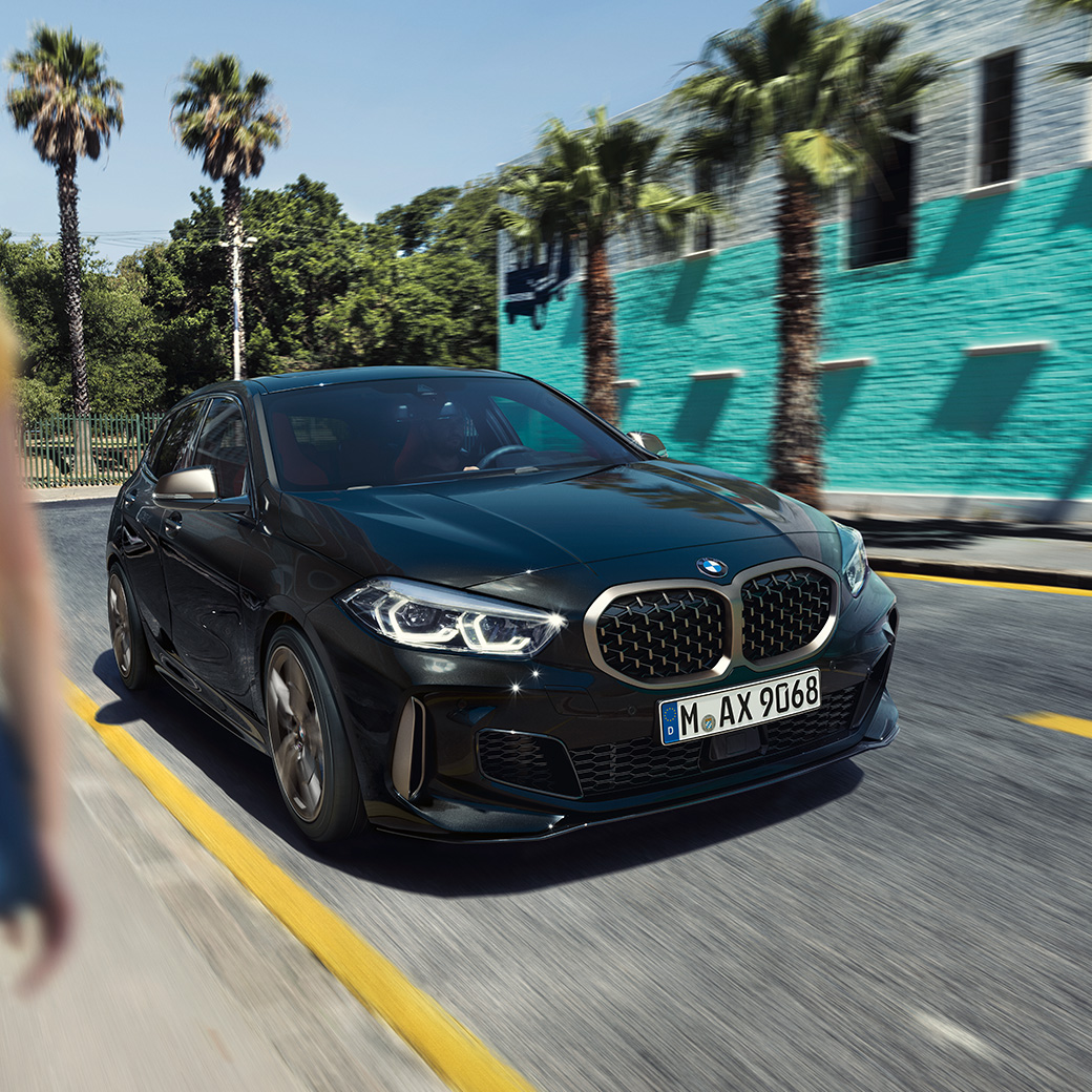 BMW M135i xDrive, vue de trois quarts avant F40. BMW M135i xDrive en Saphirschwarz metallic, vue de trois quarts avant, avec femme à l’avant-plan F40.