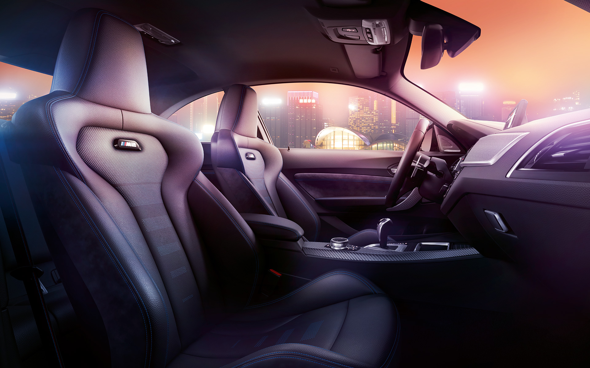 BMW M2 Competition sportzetels Cockpit en M sportzetels van de BMW M2 Competition, nachtelijke skyline op de achtergrond.