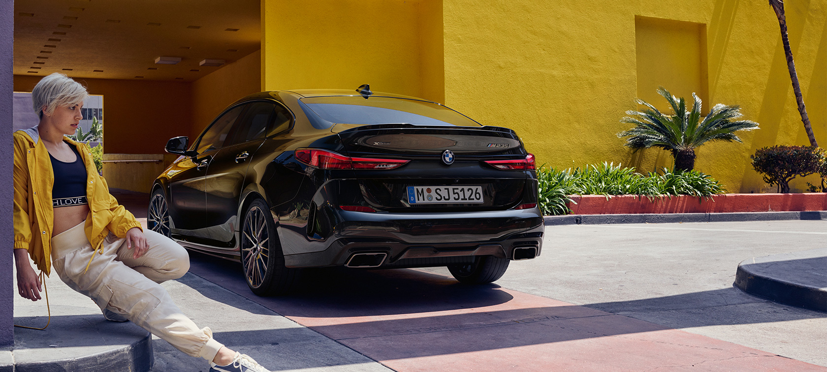BMW M235i xDrive Gran Coupé driekwart achteraanzicht BMW M235i xDrive Gran Coupé Saphirschwarz metallic F44 driekwart achteraanzicht met vrouw op de voorgrond