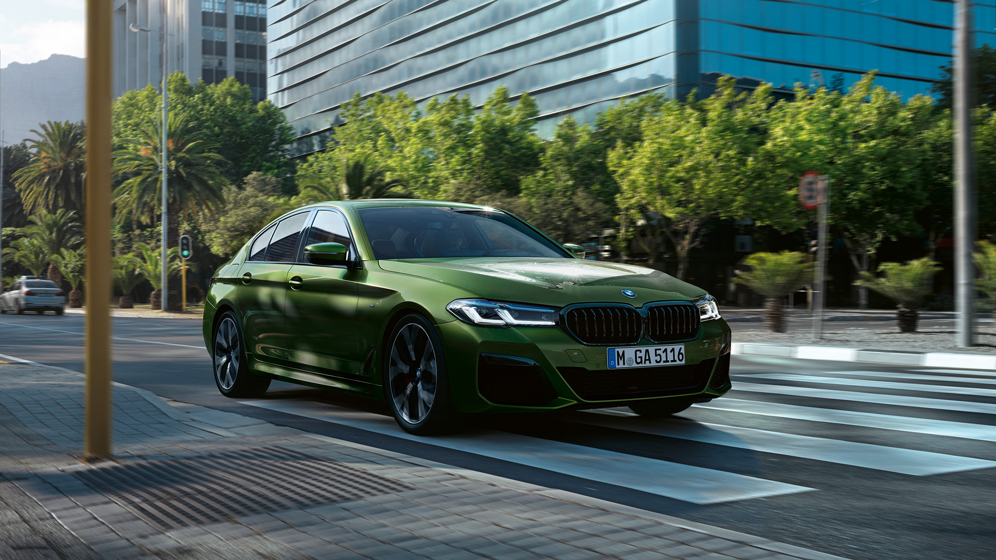 BMW M550i xDrive Berline G30 LCI facelift 2020 driekwart vooraanzicht rijdend BMW M550i xDrive Berline G30 LCI facelift 2020 BMW Individual Verde Ermes metallic driekwart vooraanzicht rijdend in de stad