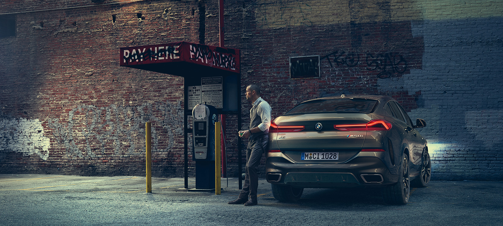 Achterkant van de BMW X6 M50i. Man leunt tegen de achterkant van de BMW X6 M50i.