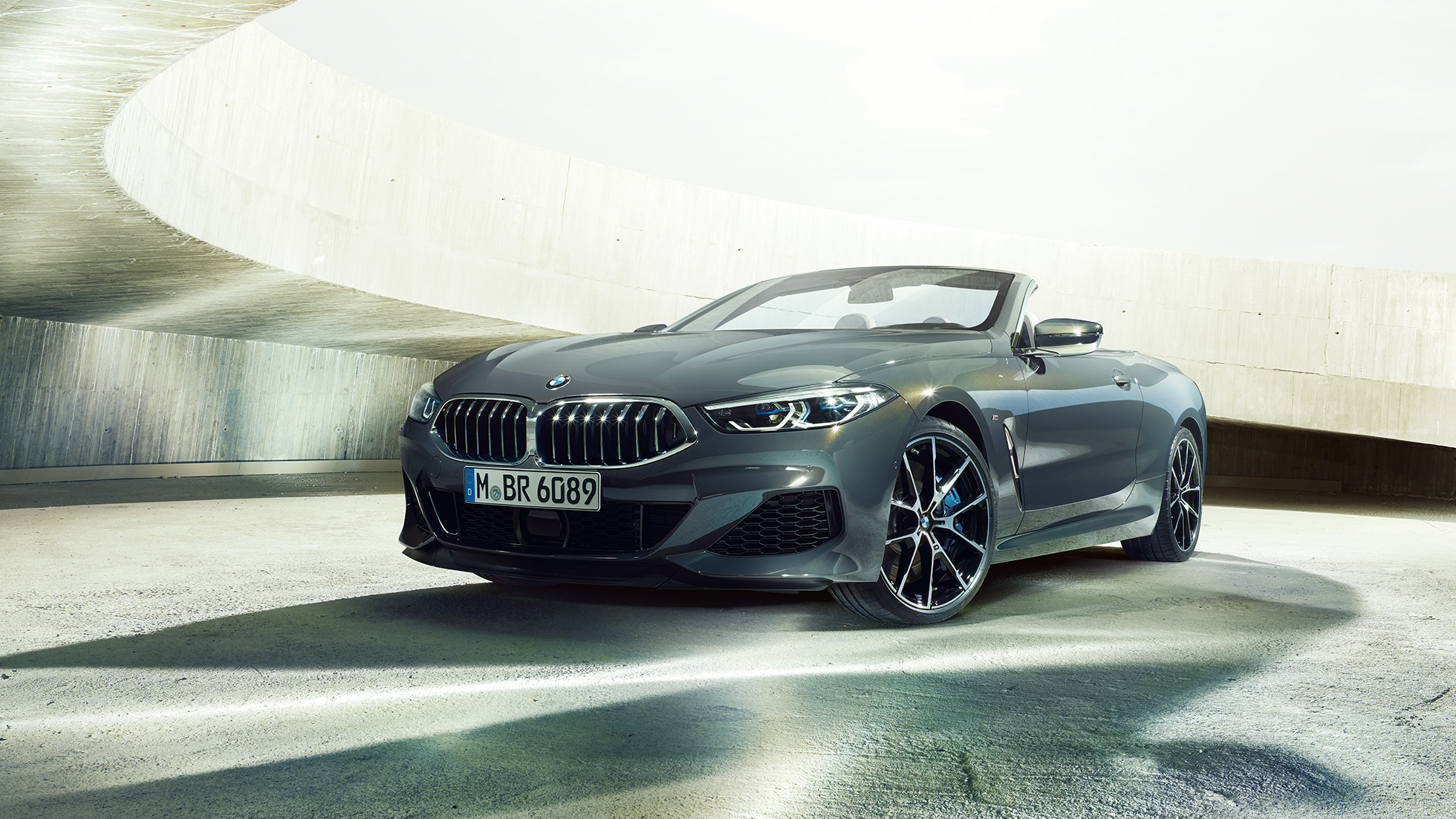BMW M850i xDrive Cabrio, vue de trois quarts avant G14. BMW M850i xDrive Cabrio en Dravitgrau metallic avec capote ouverte, vue de trois quarts avant, à l’arrêt dans un bâtiment en béton G14.