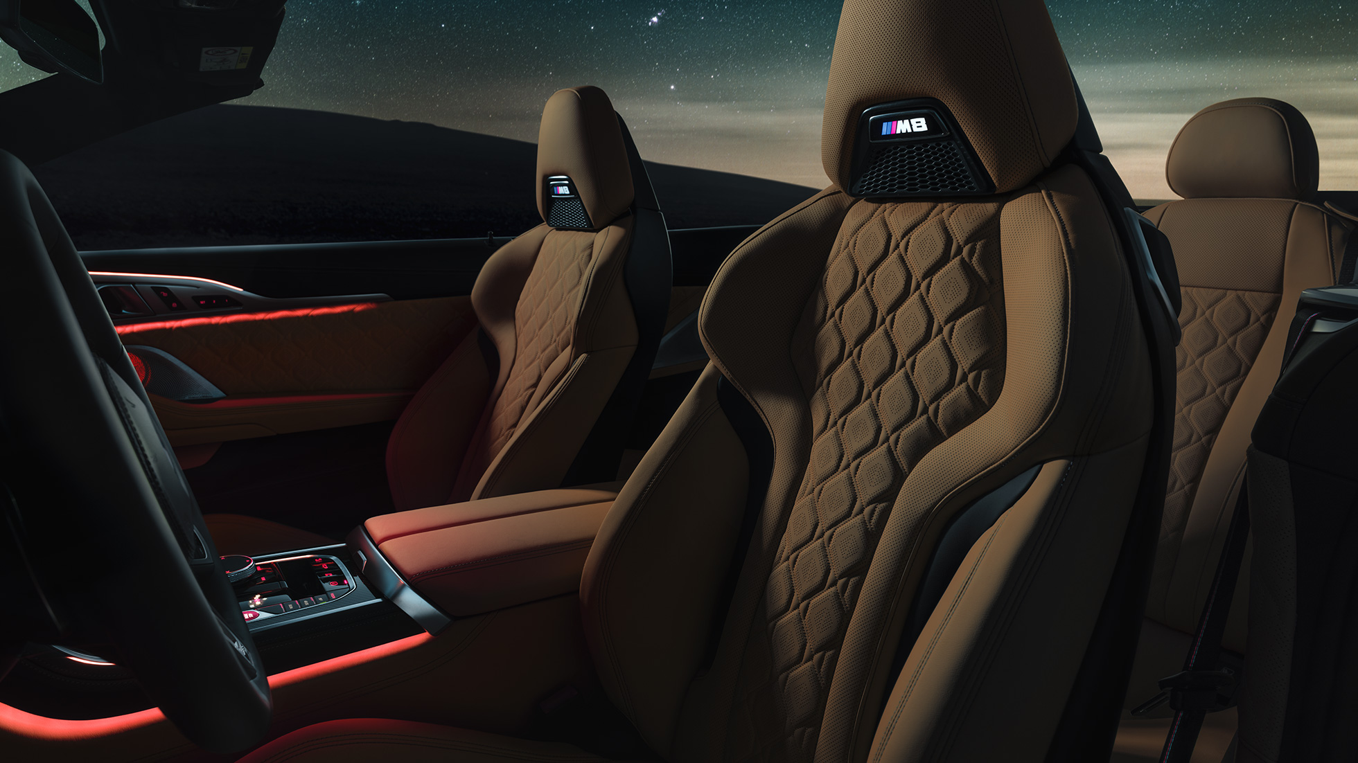 Siège M sport en cuir Merino F91. BMW M8 Competition Cabrio avec capote ouverte sous un ciel étoilé, habitacle avec sièges M sport en cuir Merino et éclairage d’ambiance rouge F91.