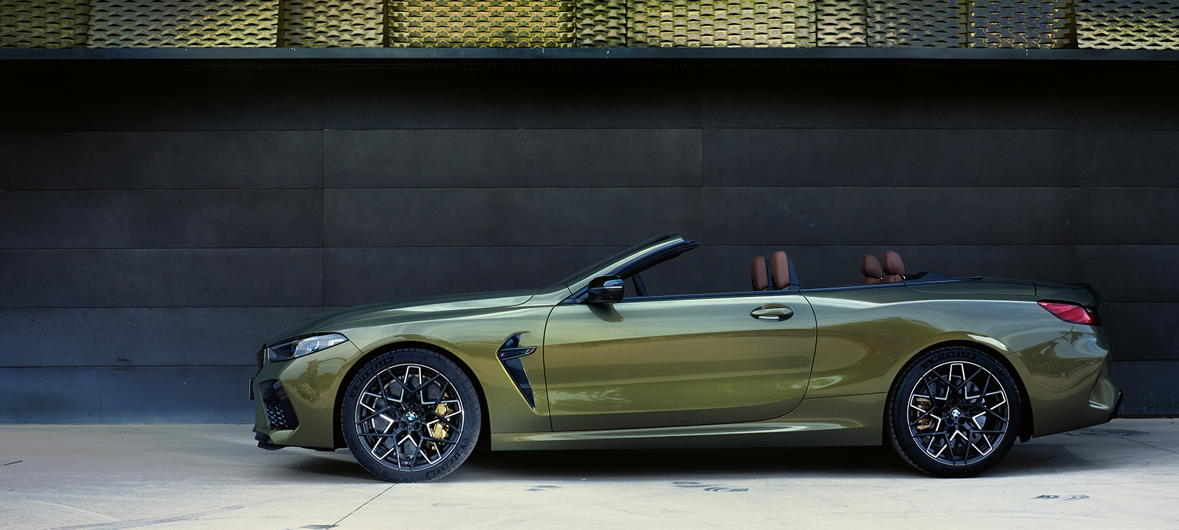 BMW M8 Competition Cabrio F91 LCI facelift 2022 zijaanzicht stilstaand BMW M8 Competition Cabrio F91 LCI facelift 2022 BMW Individual Brass metallic zijaanzicht stilstaand met geopende deur en vrouwelijk model