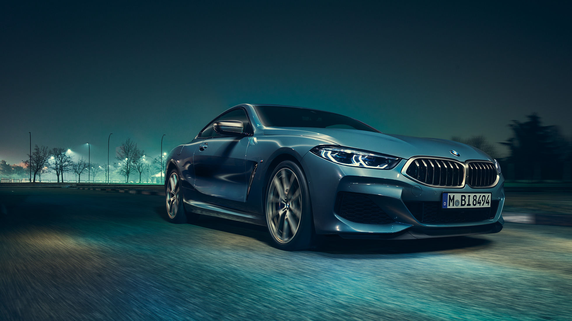 BMW M850i xDrive Coupé, driekwart vooraanzicht links G15. BMW M850i xDrive Coupé in Barcelona Blau metallic, driekwart vooraanzicht links, in beweging ‘s nachts G15.
