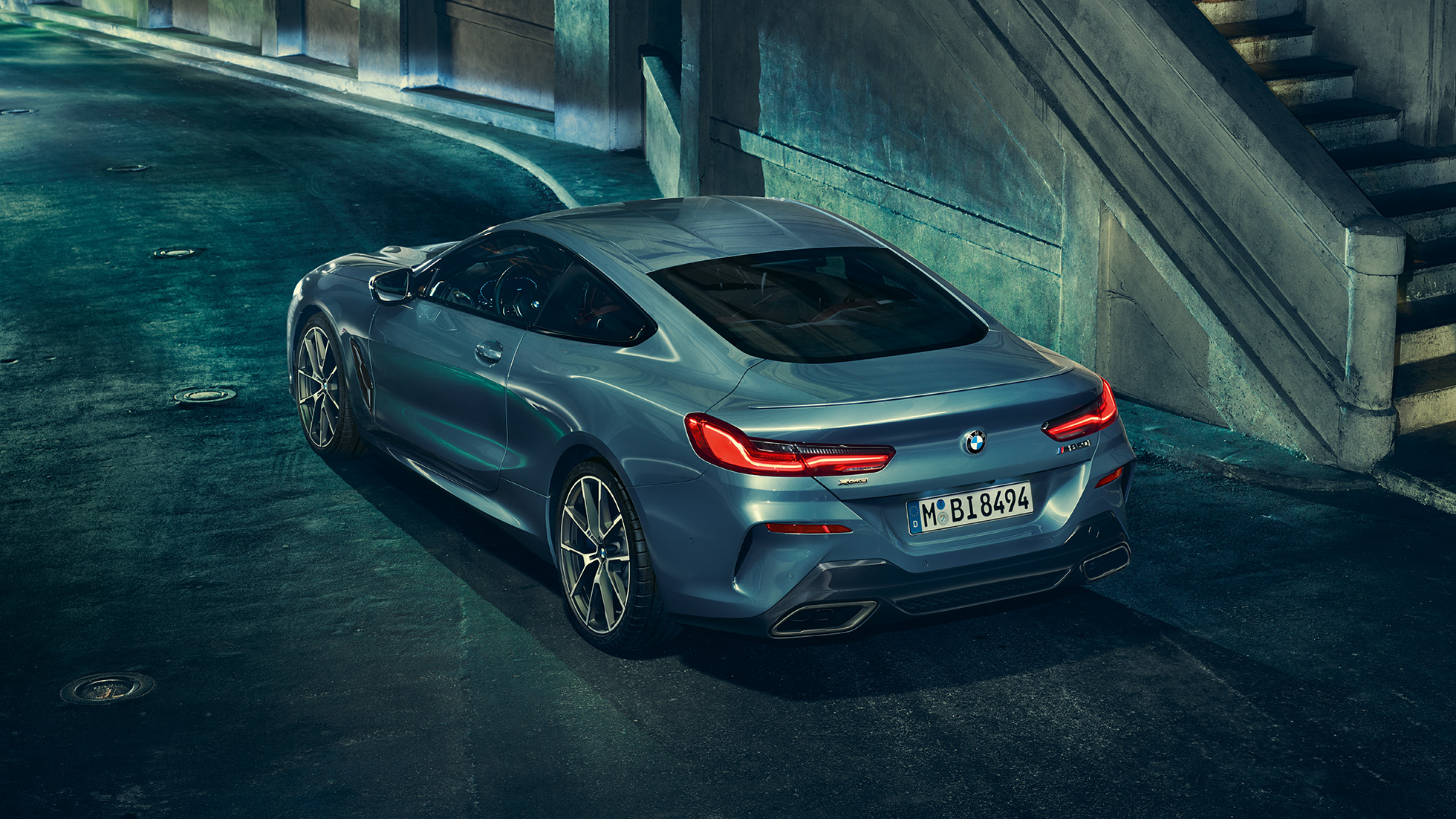 BMW M850i xDrive Coupé, driekwart achteraanzicht links G15. BMW M850i xDrive Coupé in Barcelona Blau metallic, driekwart achteraanzicht links, stilstaand ‘s nachts G15.