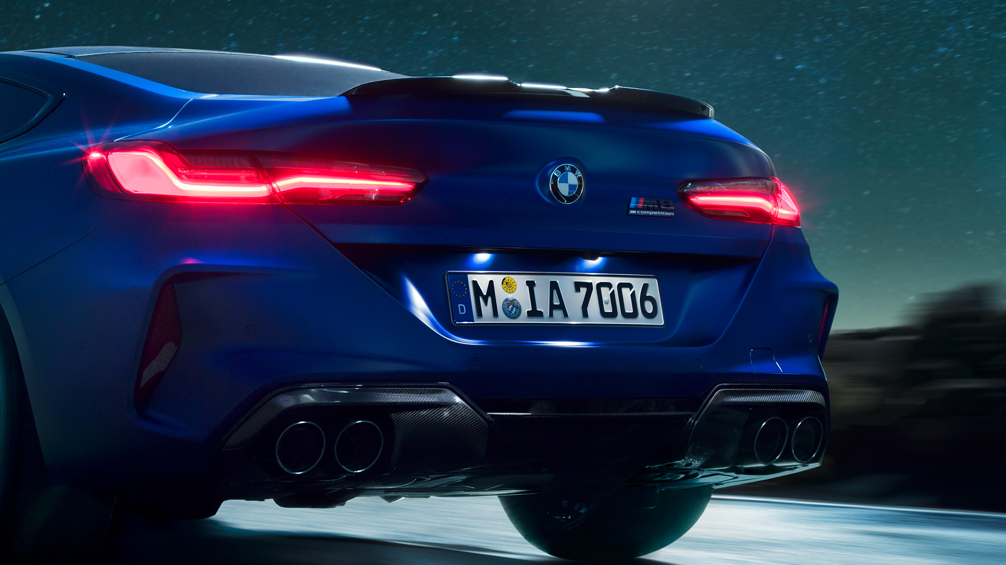 M diffusor in Carbon Schwarz F92. BMW M8 Competition Coupé in Marina Bay Blau metallic, close-up achterkant ‘s nachts met M diffusor in Carbon Schwarz F92.