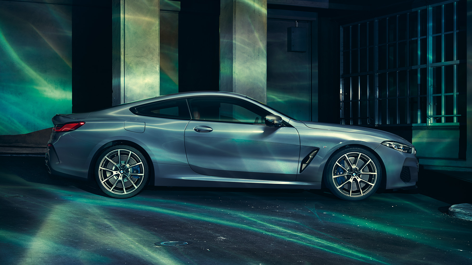 BMW M850i xDrive Coupé, zijaanzicht G15. BMW M850i xDrive Coupé in Barcelona Blau metallic, zijaanzicht stilstaand voor gebouw G15.