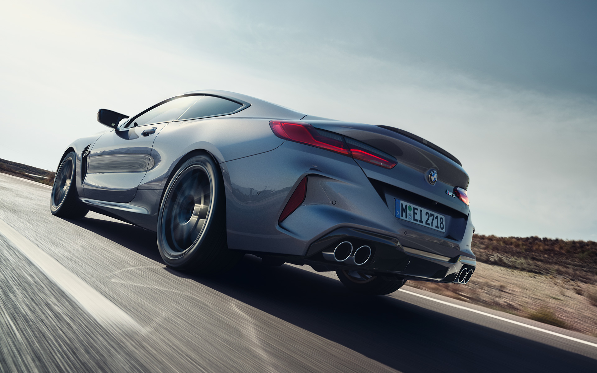 Driekwart achteraanzicht BMW M8 Coupé F92 LCI facelift 2022 rijdend op landweg BMW M8 Coupé F92 LCI facelift 2022 Skyscraper Grau metallic driekwart achteraanzicht rijdend op landweg kikvorsperspectief