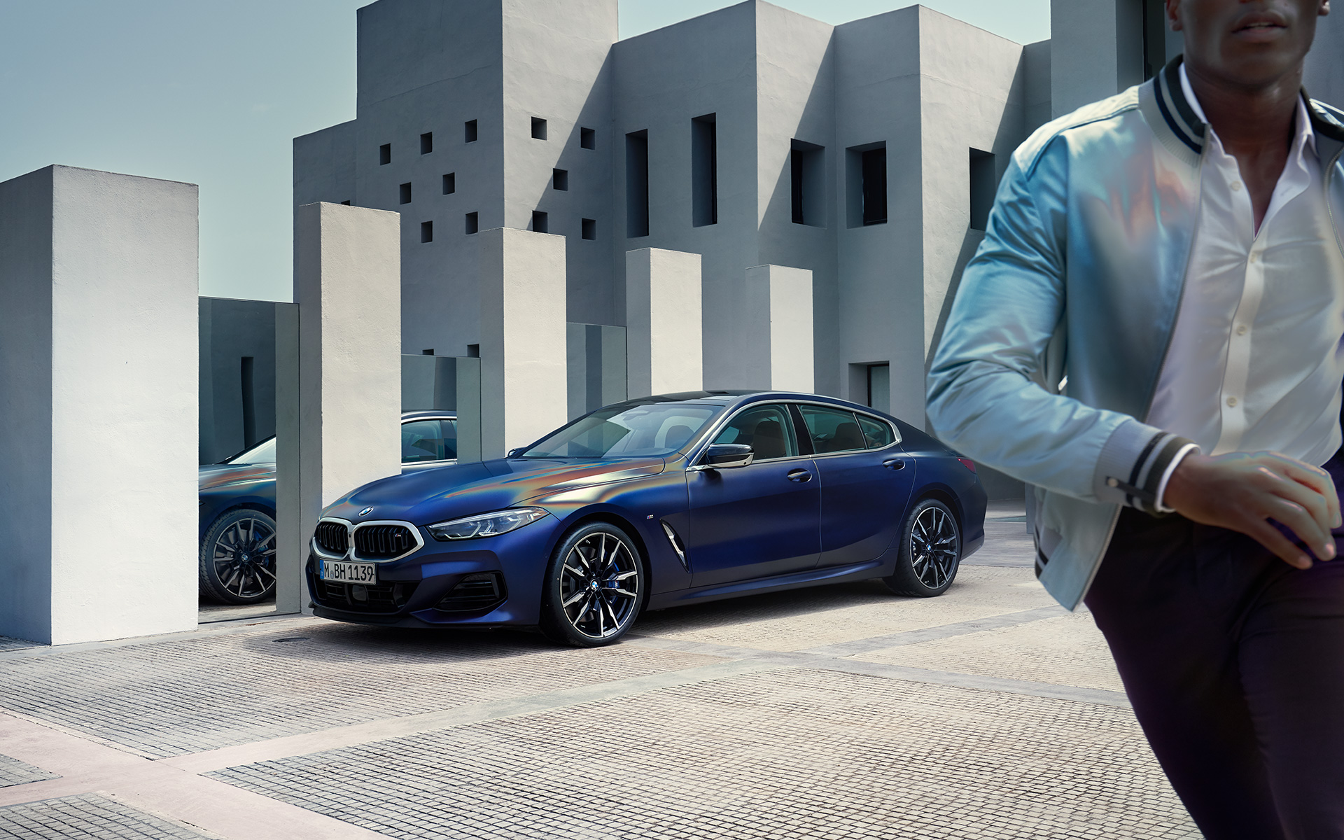 Driekwart vooraanzicht BMW M850i xDrive Gran Coupé G16 LCI facelift 2022 BMW M850i xDrive Gran Coupé G16 LCI facelift 2022 BMW Individual Frozen Tansanitblau metallic driekwart vooraanzicht stilstaand met mannelijk model op de voorgrond