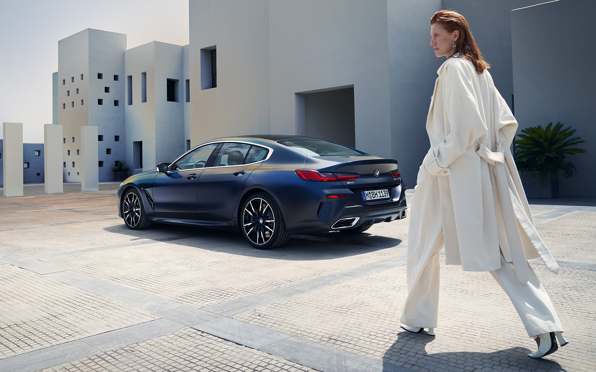 BMW M850i xDrive Gran Coupé G16 LCI facelift 2022 zijaanzicht met vrouwelijk model BMW M850i xDrive Gran Coupé G16 LCI facelift 2022 BMW Individual Frozen Tansanitblau metallic driekwart achteraanzicht met vrouwelijk model
