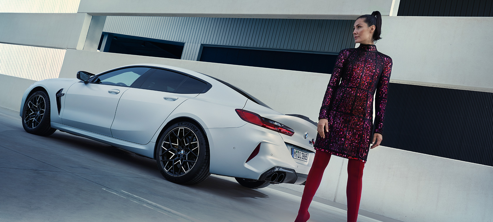 Driekwart achteraanzicht BMW M8 Competition Gran Coupé F93 LCI 2022 BMW M8 Competition Gran Coupé F93 LCI facelift 2022 BMW Individual Frozen Brilliant White metallic driekwart achteraanzicht met vrouwelijk model naast wagen