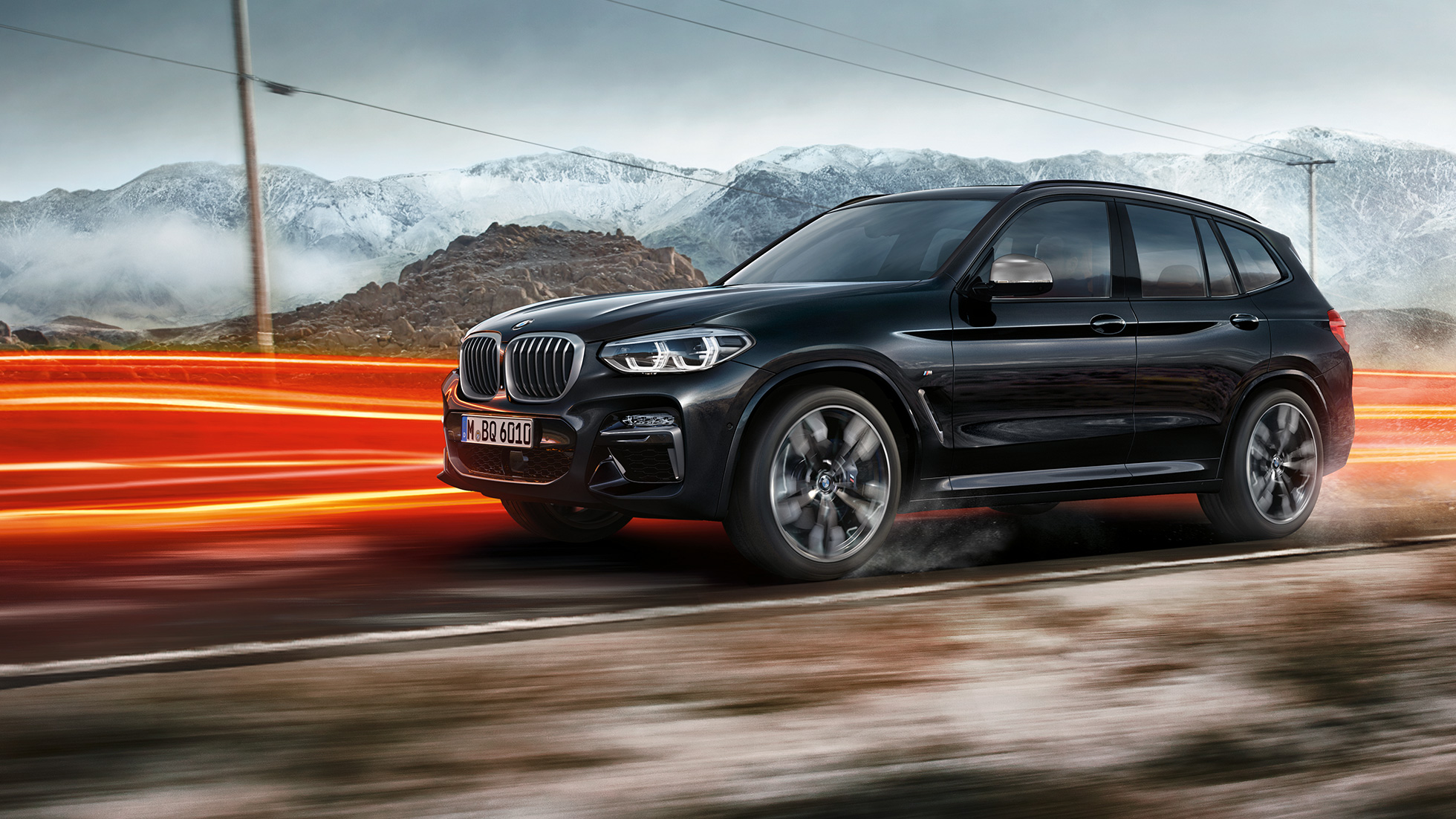 BMW X3 M40i et BMW X3 M40d, vue de profil G01. Extérieur des BMW X3 M40i et BMW X3 M40d en Saphierschwarz metallic, en mouvement, vue de profil devant un paysage montagneux avec bandes lumineuses G01.