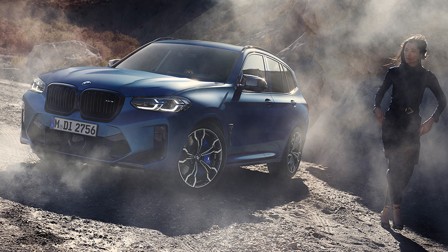 BMW X3 M Competition F97 LCI 2021 driekwart vooraanzicht stilstaand op steenachtig terrein BMW X3 M Competition F97 LCI facelift 2021 Frozen Marina Bay Blau metallic driekwart vooraanzicht stilstaand op steenachtig terrein met vrouwelijk model