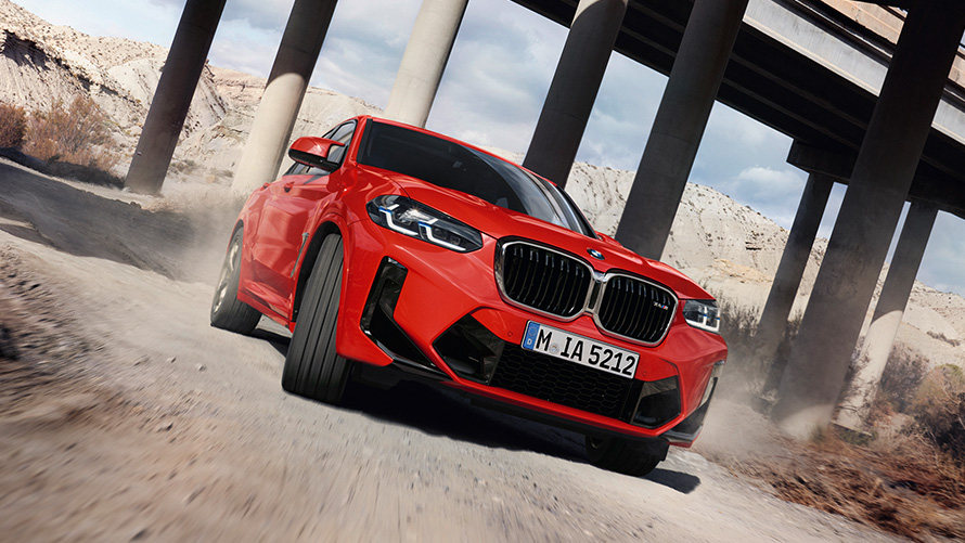 BMW X4 M F98 LCI Facelift 2021 Toronto Rot metallic vue de trois quarts avant devant les colonnes d’un pont