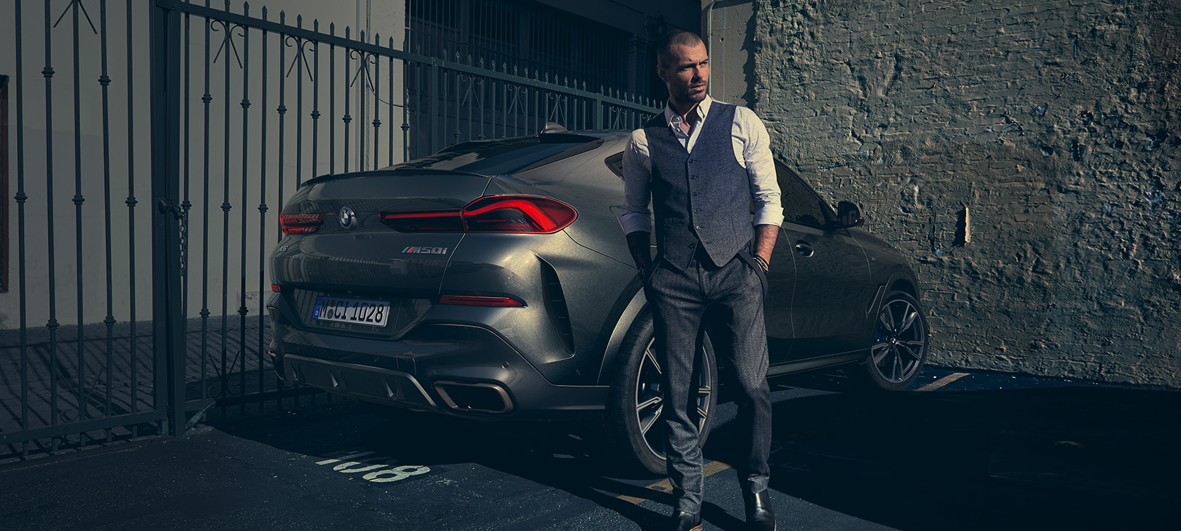 BMW X6 M50i SUV vue de trois quarts arrière. Homme debout à côté d’une BMW X6 M50i SUV vue de trois quarts arrière.