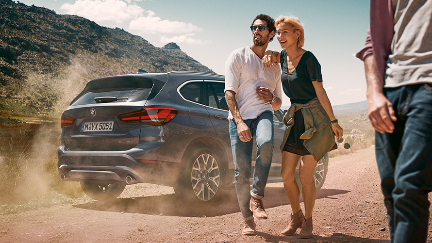 BMW X1 F48 LCI Storm Bay, vue de trois quarts arrière BMW X1 F48 LCI Storm Bay, vue de trois quarts arrière à l’arrêt dans un paysage avec des personnes devant